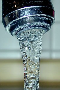 Close-up of water flowing from a faucet, with visible bubbles in the stream.