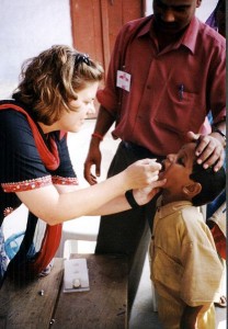 A woman administers oral drops to a young boy while a man assists, during a health check.