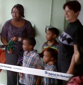 Two women and three children stand behind a Habitat for Humanity ribbon at an event.
