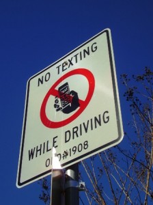 Street sign reads "No Texting While Driving" with a crossed-out phone graphic.