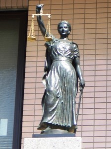 Statue of Lady Justice holding scales and a sword in front of a brick wall.