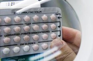 A hand holds a blister pack of birth control pills seen through a magnifying glass.