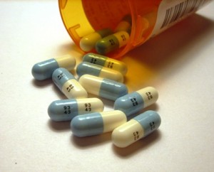 Blue and white capsules spilled from an orange prescription bottle onto a white surface.