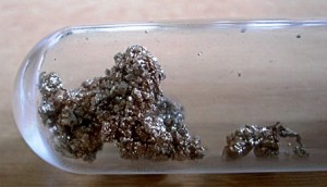 Small clumps of metallic substance inside a transparent glass test tube.