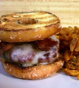 A cheeseburger with bacon uses two glazed donuts as buns, served with onion rings.