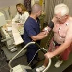 Older man undergoing a cardiac stress test on a treadmill, monitored by medical staff.