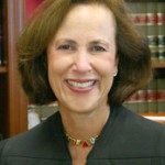 Woman in a black robe smiling in front of bookshelves filled with legal books.