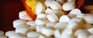 White tablets spilling out of an orange prescription bottle onto a wooden surface.