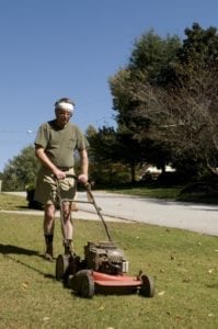 Older man mowing grass with a push lawn mower on a sunny day in a suburban neighborhood.