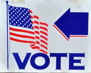 Sign with a waving American flag, a large blue arrow, and the word "VOTE" in bold letters.