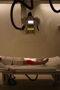 Person lying on a table under an x-ray machine with a red light over their knee.