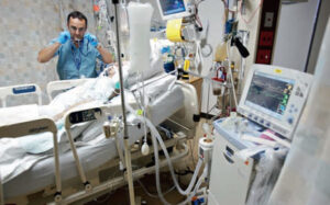 Medical professional attends to a patient on a ventilator in a hospital intensive care unit.