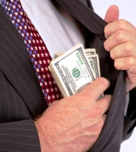 Man in suit putting a stack of U.S. dollar bills into his jacket pocket.