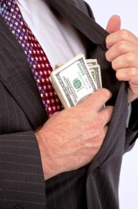 Man in suit placing a stack of hundred dollar bills into his jacket pocket.