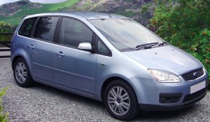 A silver Ford C-Max parked on a gravel surface with green hills in the background.