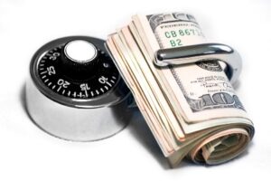A combination lock next to a rolled stack of U.S. dollar bills secured with a metal clip.