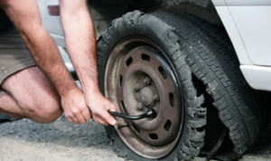 Person changing a flat, shredded tire on a car using a tire iron.