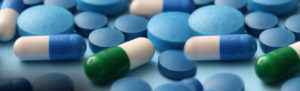 Various blue and white pills and green capsules scattered on a flat surface.