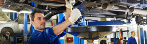 Mechanic in blue uniform working under a raised car, like a Florida product liability attorney at work.