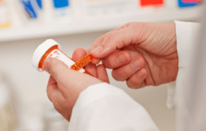 Person holding a prescription pill bottle and reading the label in a pharmacy setting.
