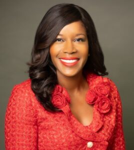 Woman in a red textured jacket smiling in front of a plain gray background.