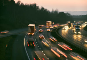 Blurred lights of cars and trucks speeding on a highway at dusk.