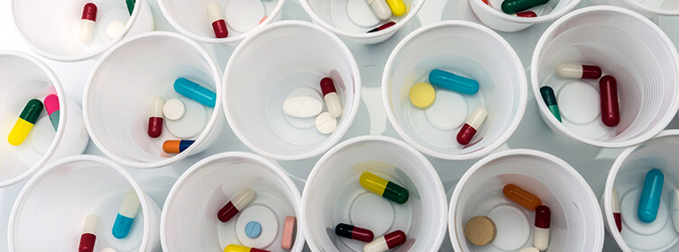 White plastic cups containing various colorful pills and capsules arranged on a flat surface.