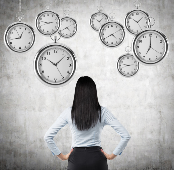 A rear view of a brunette business lady who is looking at the hovering pocket watches in the air. A concept of a value of time in business. Concrete background.