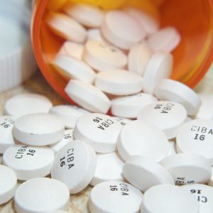 White pills labeled “CIBA 16” spilled from an orange prescription bottle onto a surface.