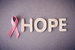 The word "HOPE" with a pink ribbon replacing the letter "O" on a gray background.