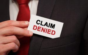 Person in suit holding an "Irma commercial claims DENIED" card in black and red text.