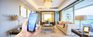 Person holds smartphone controlling smart home features in a modern, bright living room.
