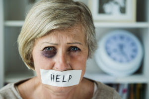 Older woman with a black eye and tape labeled "HELP" over her mouth, looking at camera.
