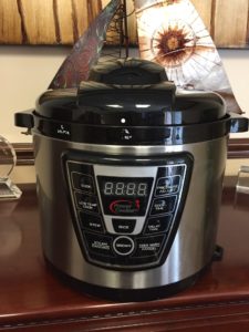 A stainless steel pressure cooker with control panel sits on a wooden surface—dangerous if misused.