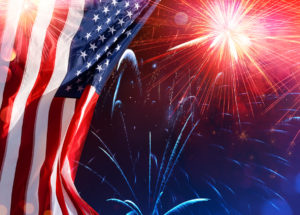 An American flag with colorful fireworks in the night sky in the background.