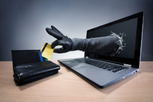 A gloved hand reaches out of a laptop, symbolizing online identity theft and credit card fraud.