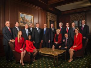 A group of professionally dressed men and women pose together in a formal wood-paneled office.