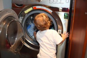 A young child looks into the open door of a front-loading washing machine.