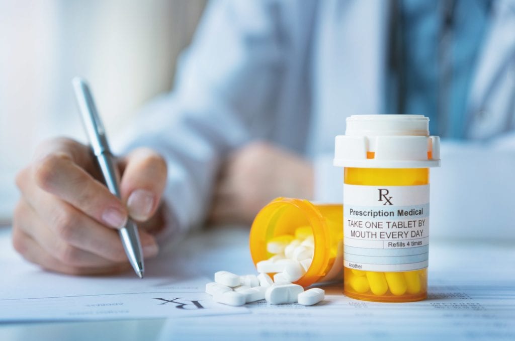 Doctor signing prescription next to bottle of pills