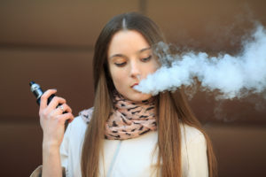 Woman with long hair vaping, exhaling a large cloud of vapor, holding a vape device.