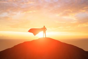 Silhouette of a person in a cape standing on a hilltop at sunrise or sunset.