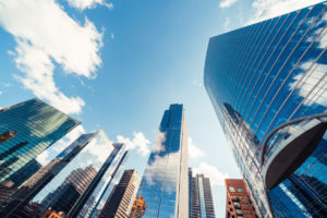 Tall modern skyscrapers with glass facades under a blue sky with scattered clouds.