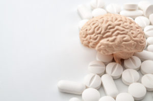 Plastic brain model surrounded by white pills on a white background.