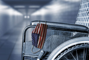 Close-up of a wheelchair with a USA flag face mask hanging from the armrest in a hallway.