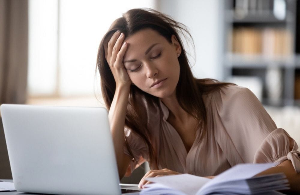 A young, fatigued woman rests her head on her hand while working at her laptop. Severe fatigue is a symptom of both iron deficiency anemia and severe hypophosphatemia.