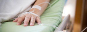 A person's hand with an IV line rests on a hospital bed—contact a Florida Catastrophic Injury Lawyer.