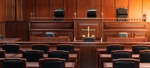 Empty courtroom with wooden benches, judge’s bench, and a scales of justice emblem.