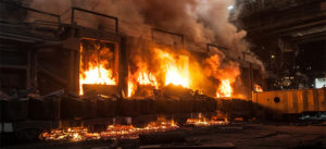 Large industrial furnace with intense flames and smoke inside a factory setting.