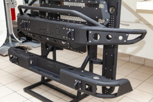 Black off-road vehicle bumpers on display stand in a showroom with tiled flooring.