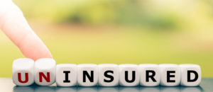 Hand pushing letter blocks spelling "UNINSURED" with "UN" highlighted in red.